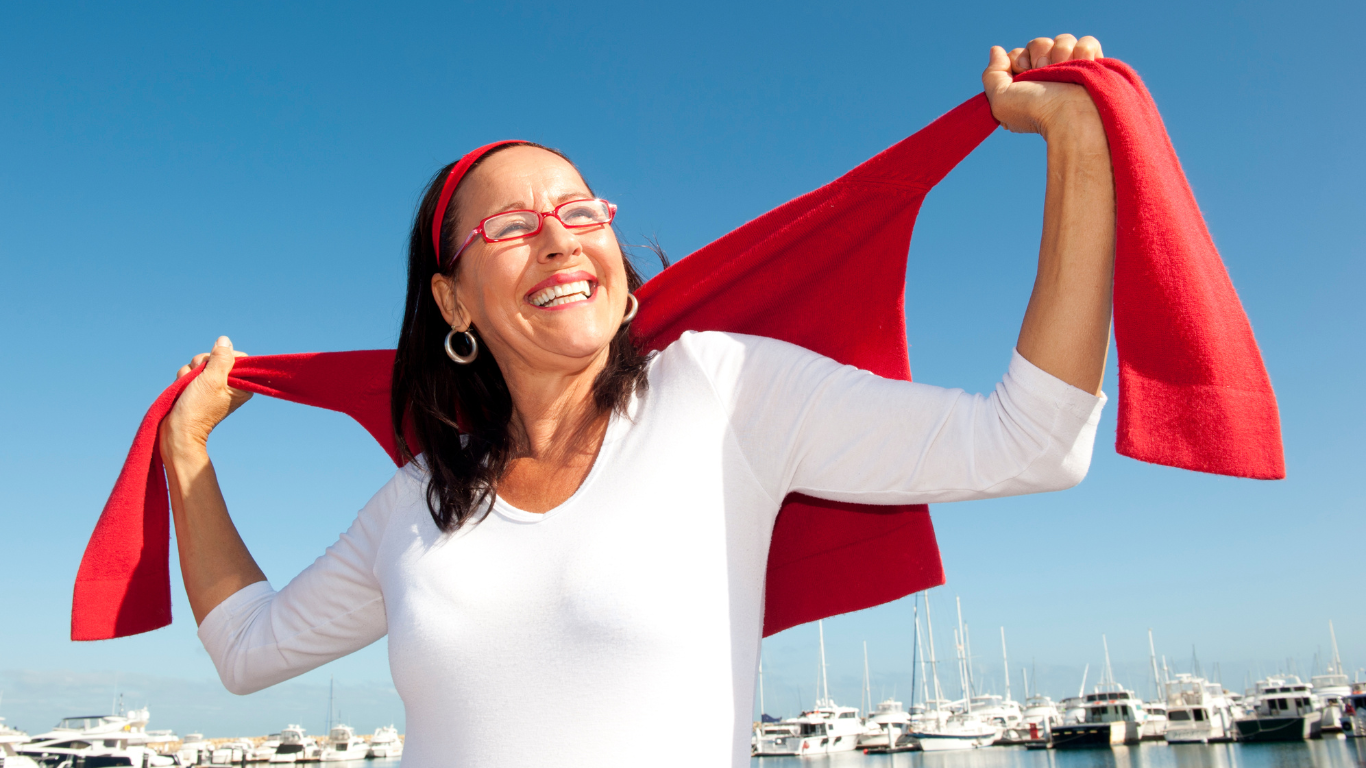 Femme en gros plan avec un pull rouge sur les épaules, ciel bleu et bateaux en arrière-plan